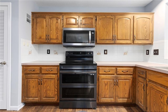 kitchen featuring backsplash, visible vents, appliances with stainless steel finishes, brown cabinets, and dark wood finished floors