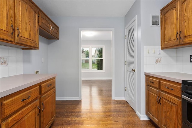 kitchen featuring light countertops, brown cabinets, tasteful backsplash, and dark wood-style floors