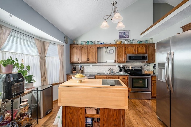 kitchen featuring vaulted ceiling, light wood-style flooring, decorative backsplash, stainless steel appliances, and a sink