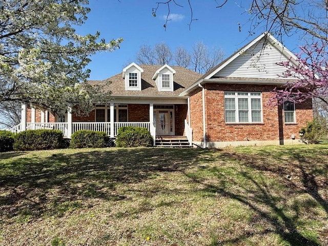 new england style home with a porch, roof with shingles, a front lawn, and brick siding
