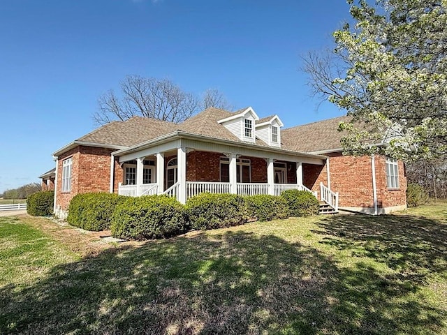 exterior space featuring a lawn, covered porch, and brick siding