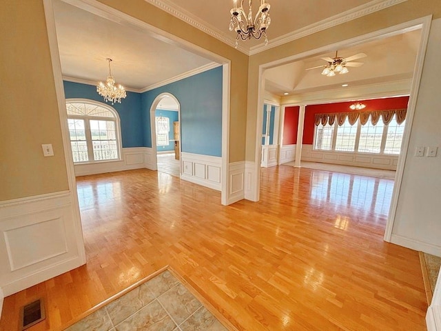 unfurnished room featuring ornamental molding, light wood-style flooring, visible vents, arched walkways, and ceiling fan with notable chandelier