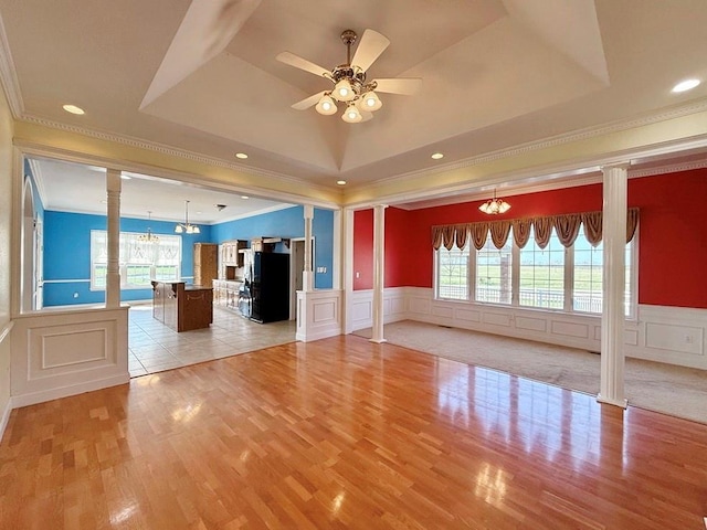 unfurnished living room featuring a tray ceiling, decorative columns, and a wealth of natural light