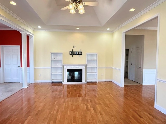 unfurnished living room with decorative columns, light wood-style floors, a tray ceiling, and ceiling fan