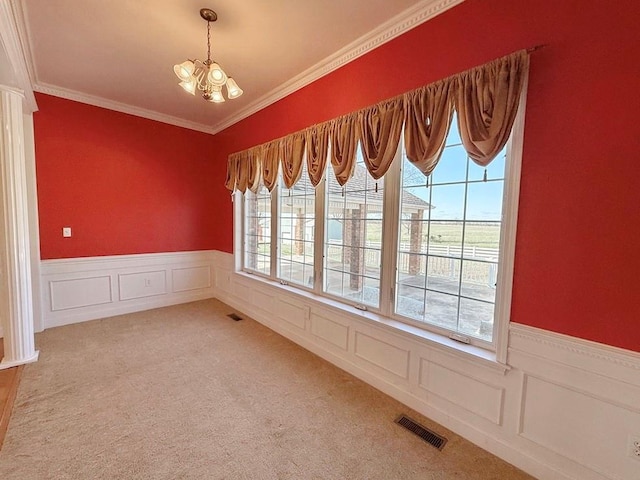 spare room featuring a notable chandelier, carpet flooring, crown molding, a wainscoted wall, and visible vents