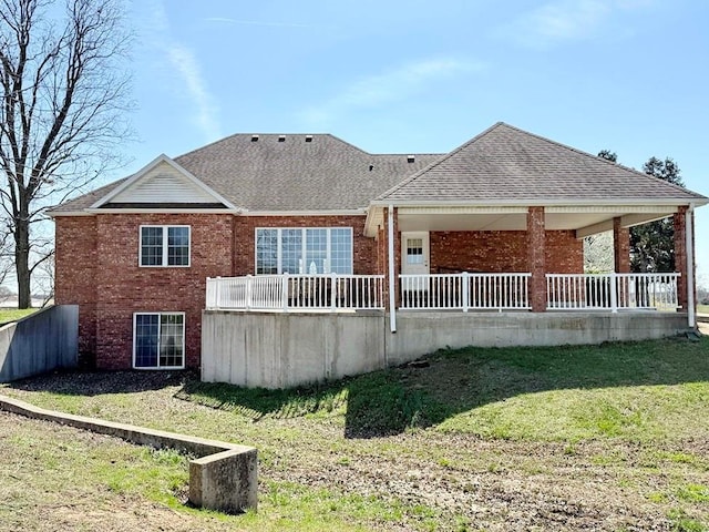 rear view of house with roof with shingles, brick siding, a lawn, and covered porch