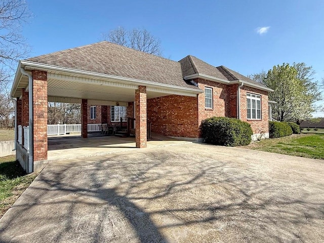 view of front facade featuring brick siding, a shingled roof, a carport, and driveway