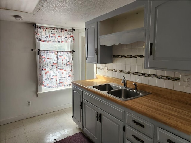 1126 S Pearl St, Independence, MO 64050 - kitchen featuring a textured ceiling, baseboards, a sink, gray cabinets, and backsplash