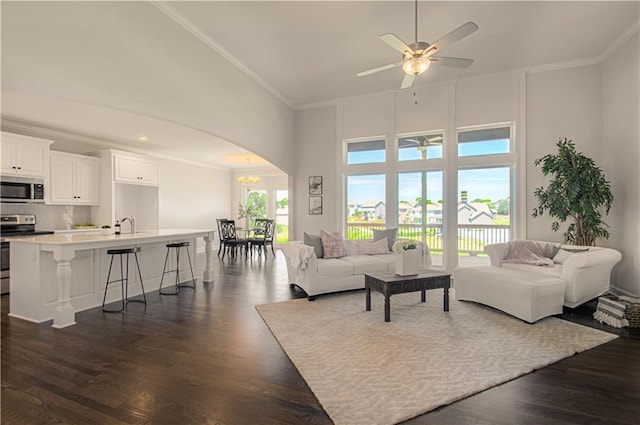 living room featuring arched walkways, dark wood-style flooring, a ceiling fan, and crown molding