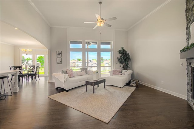 living room with dark wood-style flooring, crown molding, a towering ceiling, arched walkways, and ceiling fan with notable chandelier