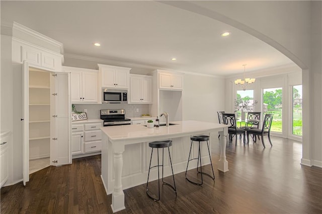 kitchen with crown molding, light countertops, appliances with stainless steel finishes, dark wood-style floors, and an inviting chandelier