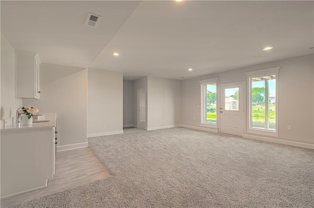 unfurnished living room featuring light colored carpet, recessed lighting, baseboards, a sink, and visible vents