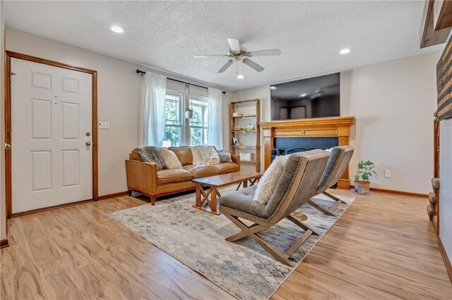 living room featuring baseboards, a textured ceiling, a ceiling fan, a fireplace, and wood finished floors