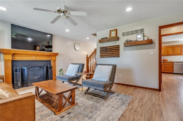 living area with stairs, a fireplace, visible vents, light wood-style floors, and ceiling fan