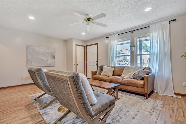 living area featuring a textured ceiling, baseboards, light wood-style flooring, and a ceiling fan