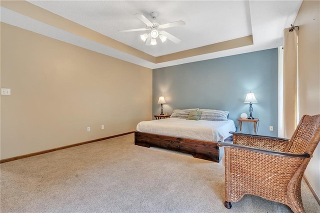 carpeted bedroom featuring a ceiling fan, a raised ceiling, and baseboards