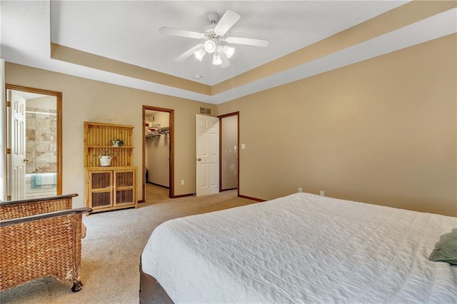 bedroom with a tray ceiling, a ceiling fan, light carpet, a spacious closet, and baseboards