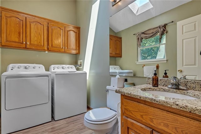 half bath with washer and clothes dryer, vaulted ceiling with skylight, toilet, vanity, and wood finished floors