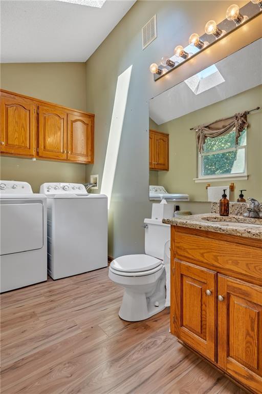 bathroom with vaulted ceiling with skylight, toilet, separate washer and dryer, wood finished floors, and visible vents
