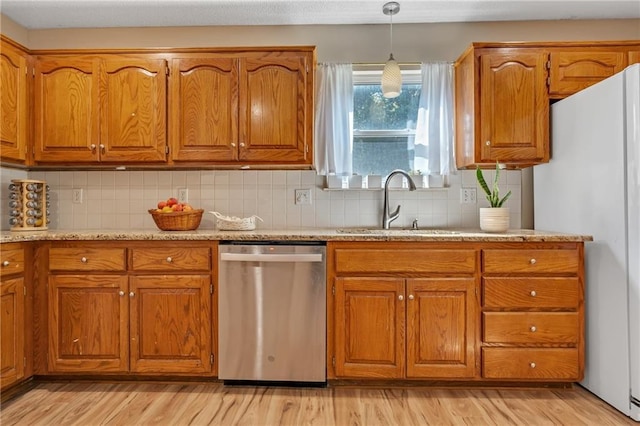 kitchen featuring a sink, brown cabinets, freestanding refrigerator, and dishwasher