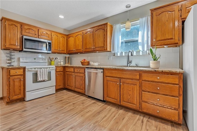 kitchen featuring a sink, appliances with stainless steel finishes, hanging light fixtures, brown cabinetry, and light wood-style flooring