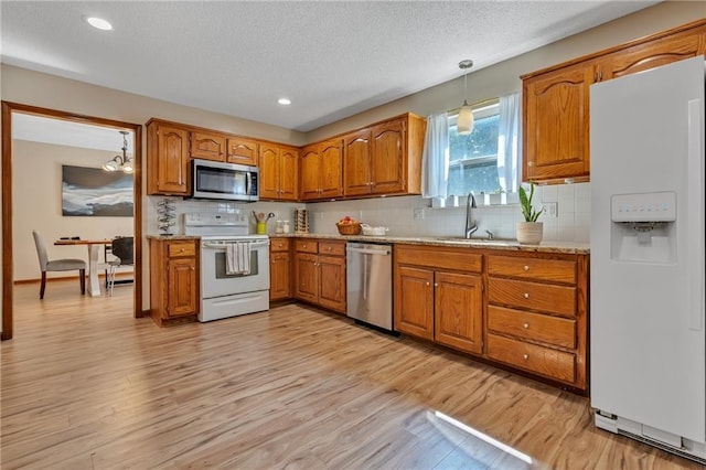 kitchen with a sink, light wood finished floors, hanging light fixtures, brown cabinets, and stainless steel appliances