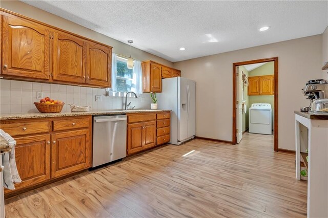 kitchen with brown cabinetry, white fridge with ice dispenser, washer / dryer, and dishwasher