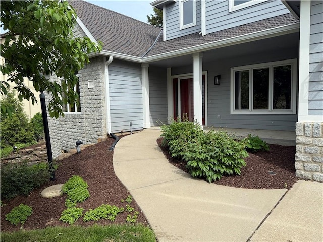 view of exterior entry featuring roof with shingles, covered porch, and stone siding