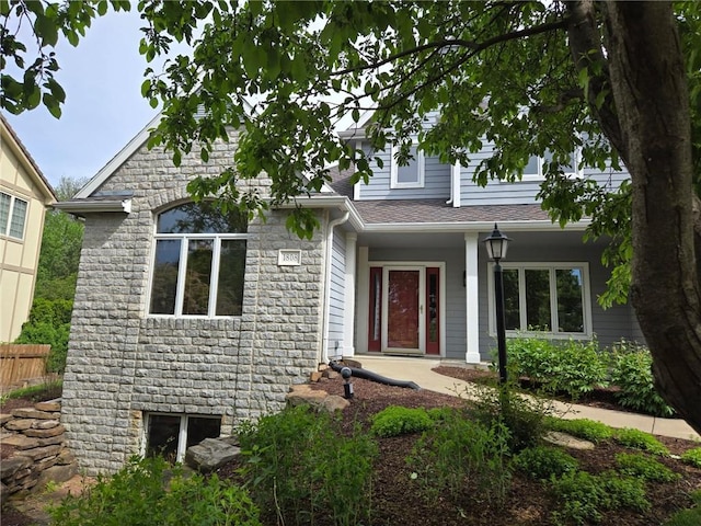 view of front of home with roof with shingles, fence, and stone siding