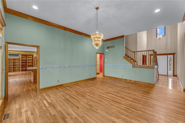 unfurnished room featuring crown molding, wood finished floors, baseboards, a chandelier, and stairs