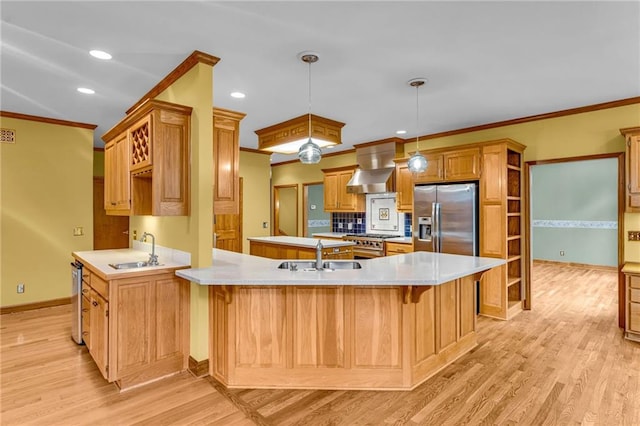 kitchen with a sink, stainless steel appliances, a peninsula, and wall chimney exhaust hood