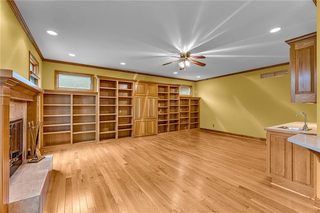 unfurnished living room with crown molding, ceiling fan, a sink, a premium fireplace, and light wood-style flooring