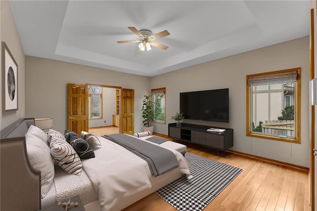 bedroom with visible vents, light wood finished floors, a tray ceiling, and multiple windows