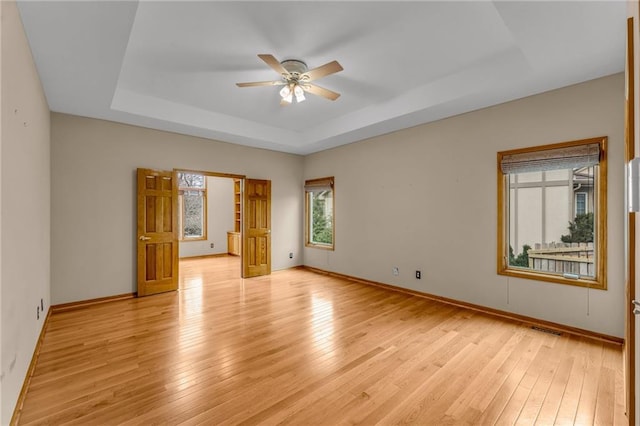empty room with light wood finished floors, a raised ceiling, a ceiling fan, baseboards, and visible vents