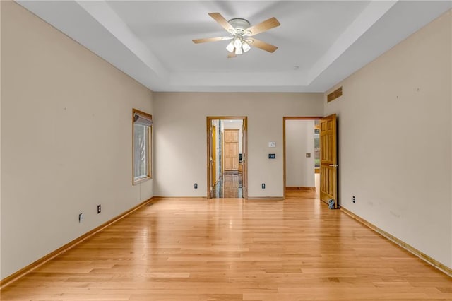 empty room with visible vents, baseboards, a tray ceiling, a ceiling fan, and light wood-style flooring