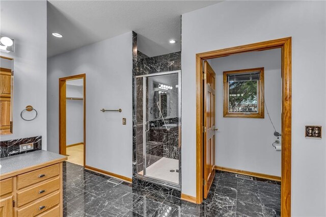 bathroom with a walk in closet, vanity, marble finish floor, baseboards, and a stall shower