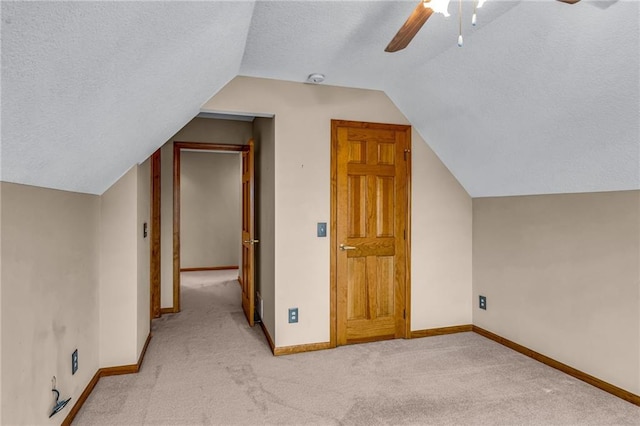 additional living space with light carpet, a textured ceiling, a ceiling fan, baseboards, and vaulted ceiling