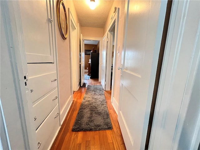 corridor featuring light wood finished floors, baseboards, and a textured ceiling
