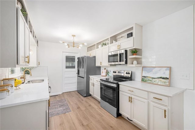 kitchen featuring appliances with stainless steel finishes, a sink, a chandelier, open shelves, and light wood-type flooring