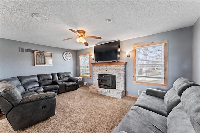 carpeted living area with a ceiling fan, a textured ceiling, visible vents, and a wood stove