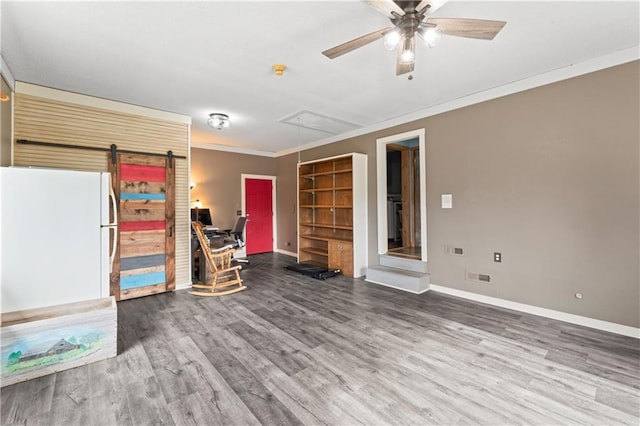 interior space with a barn door, attic access, a ceiling fan, baseboards, and wood finished floors