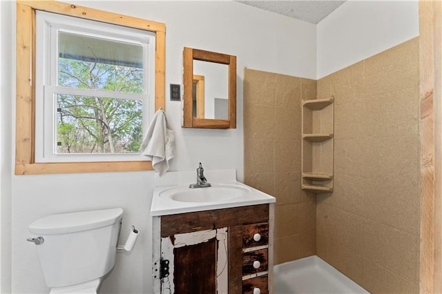 full bathroom with toilet, tiled shower, and vanity