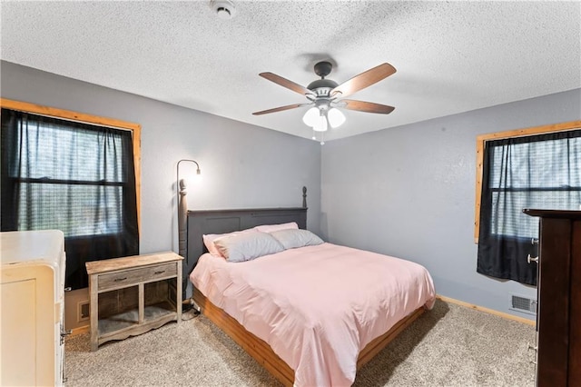 bedroom with a textured ceiling, visible vents, multiple windows, and light carpet