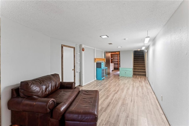 living room featuring baseboards, a textured ceiling, light wood finished floors, and stairway