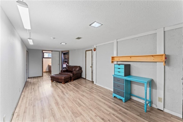 interior space with a textured wall, a textured ceiling, baseboards, wood finished floors, and visible vents