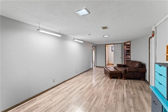 interior space with a textured ceiling, visible vents, baseboards, and light wood finished floors