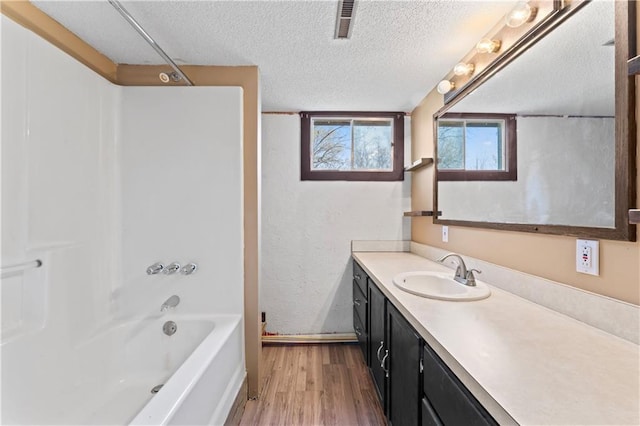 bathroom with a textured ceiling, visible vents, wood finished floors, vanity, and baseboards