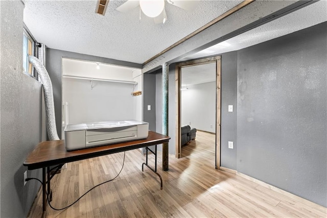 office area with a textured wall, a textured ceiling, a ceiling fan, wood finished floors, and visible vents