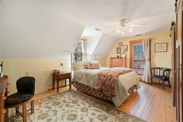 bedroom with a barn door, a textured ceiling, visible vents, and light wood-type flooring
