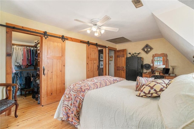 bedroom featuring a walk in closet, vaulted ceiling, light wood-type flooring, a barn door, and a closet